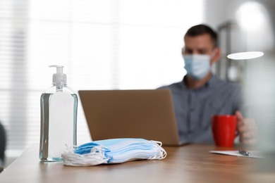 Hand sanitizer, masks and blurred view of office worker on background. Protective measures during COVID-19 pandemic