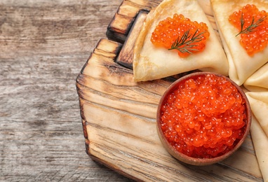 Bowl with delicious red caviar and thin pancakes on wooden board