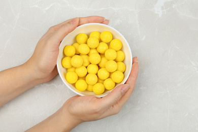 Photo of Woman holding bowl of lemon drops at light table, top view