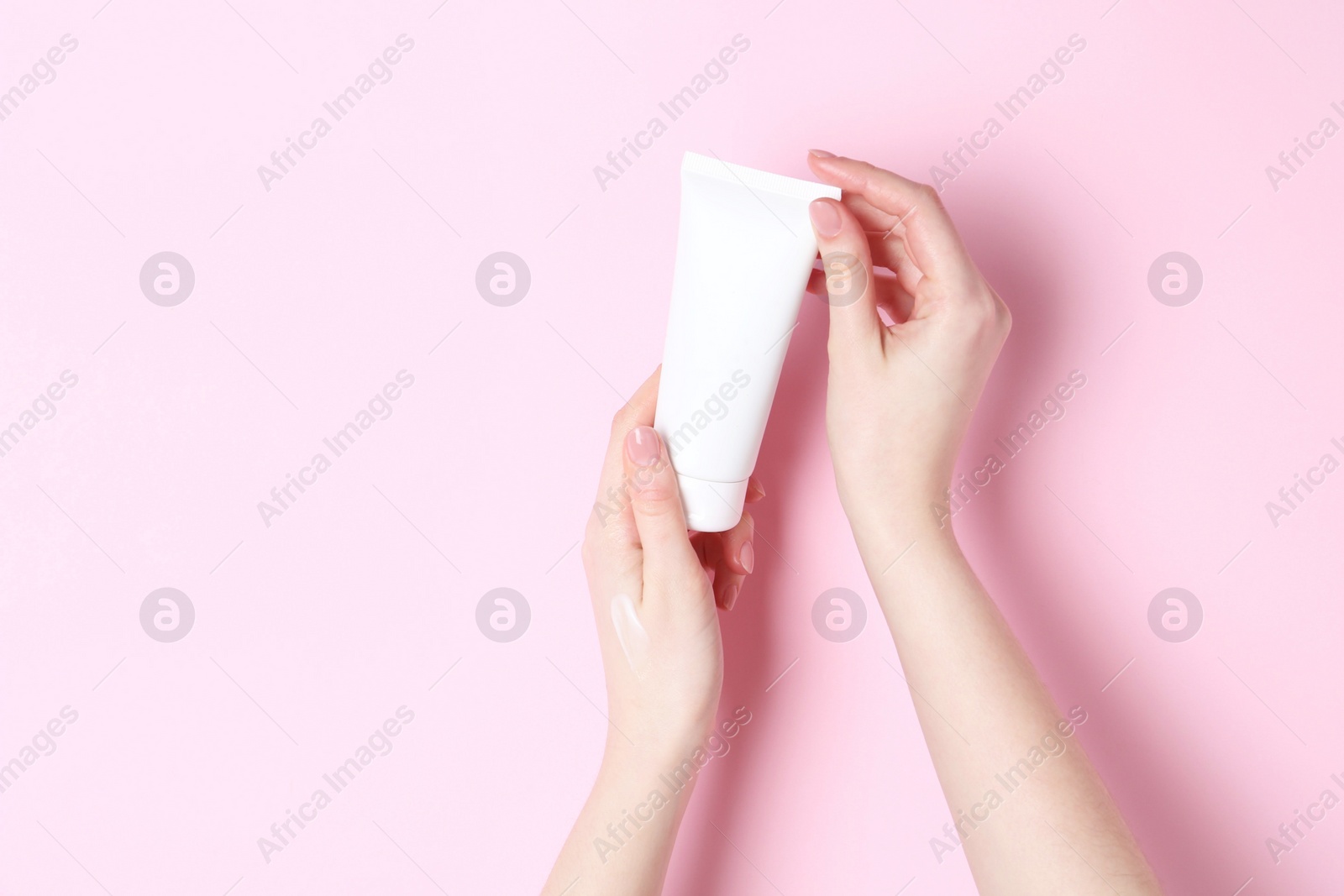 Photo of Woman holding tube of cream on pink background, closeup