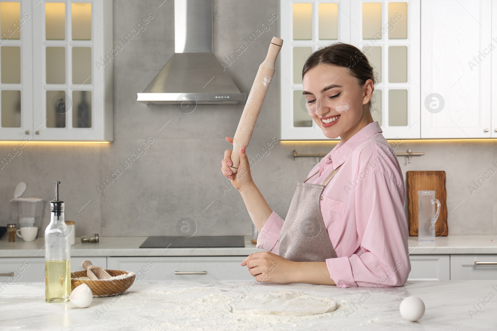 Photo of Smiling woman with soiled face holding rolling pin at messy table in kitchen