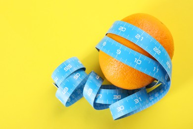 Cellulite problem. Orange with measuring tape on yellow background, top view