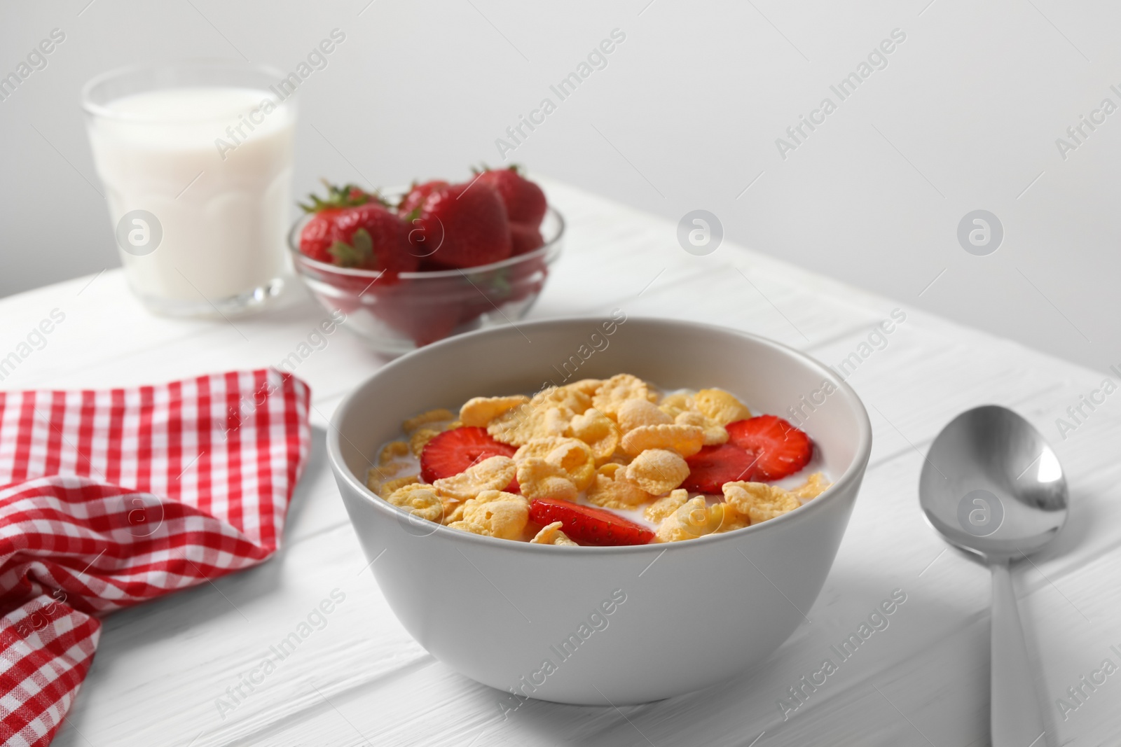 Photo of Corn flakes with strawberries in bowl served on white wooden table