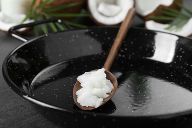 Photo of Frying pan with organic coconut cooking oil and wooden spoon on grey table, closeup