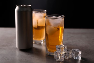 Photo of Energy drink in glasses, aluminium can and ice cubes on grey table