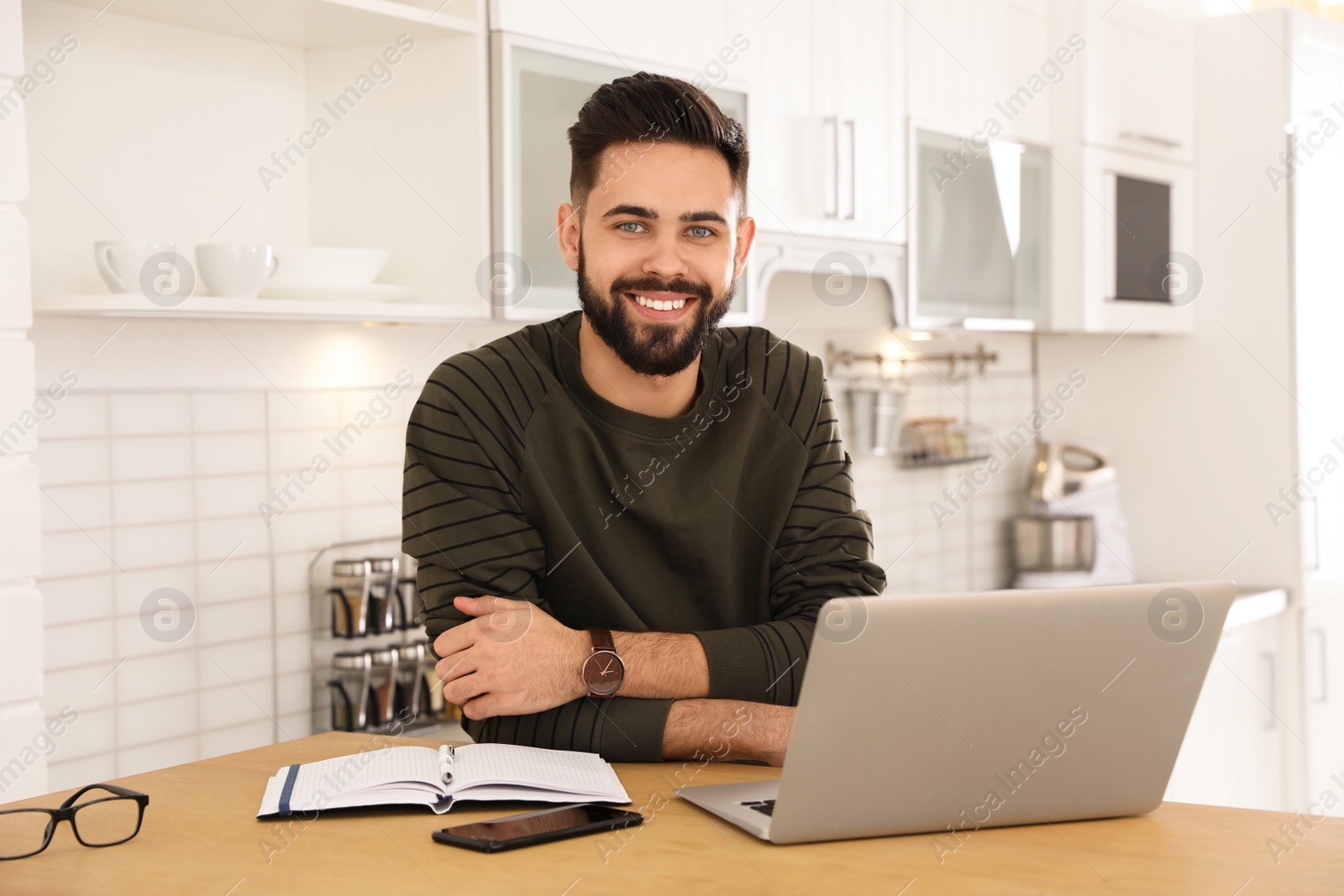 Photo of Handsome young man working with laptop at table in kitchen