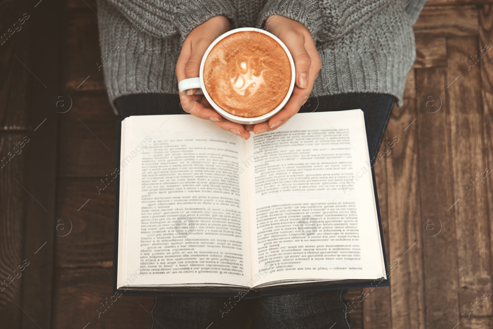 Image of Woman with cup of coffee reading book at home, top view