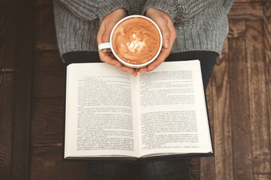 Image of Woman with cup of coffee reading book at home, top view