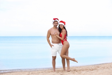 Photo of Happy young couple with Santa hats on beach near sea