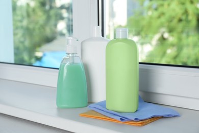 Photo of Bottles of detergents and rags on window sill indoors. Cleaning supplies