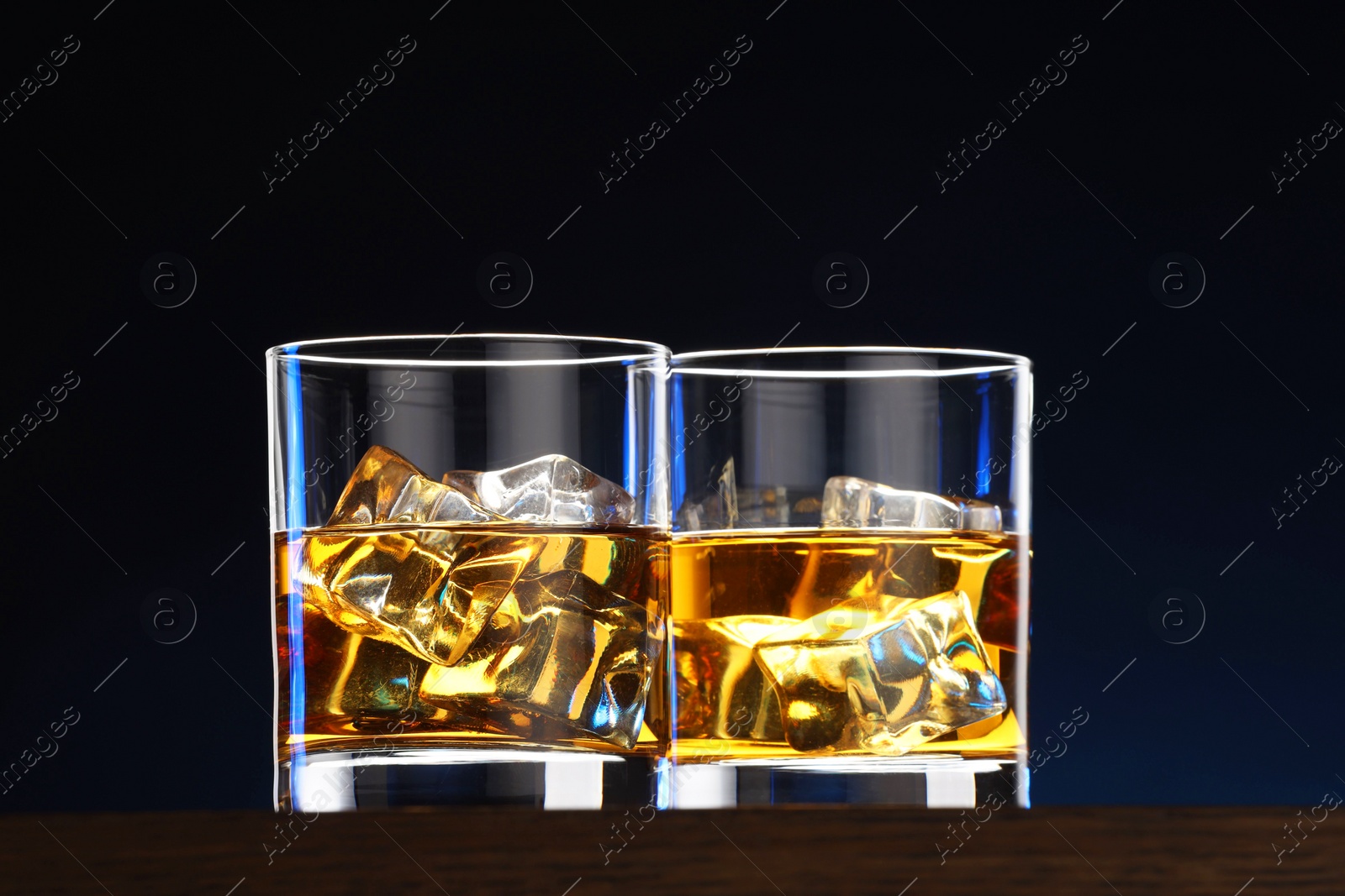 Photo of Whiskey with ice cubes in glasses on table against dark background, closeup