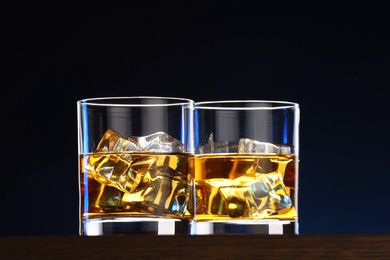 Photo of Whiskey with ice cubes in glasses on table against dark background, closeup
