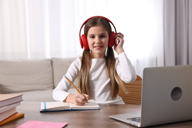 Photo of E-learning. Cute girl taking notes during online lesson at table indoors