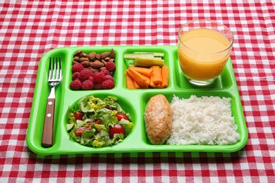 Serving tray with healthy food on checkered background. School lunch