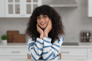 Photo of Portrait of beautiful woman with curly hair in kitchen. Attractive lady smiling and looking into camera