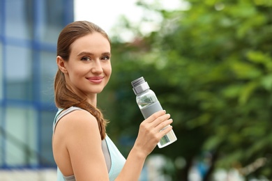 Photo of Young woman with bottle of water outdoors. Refreshing drink