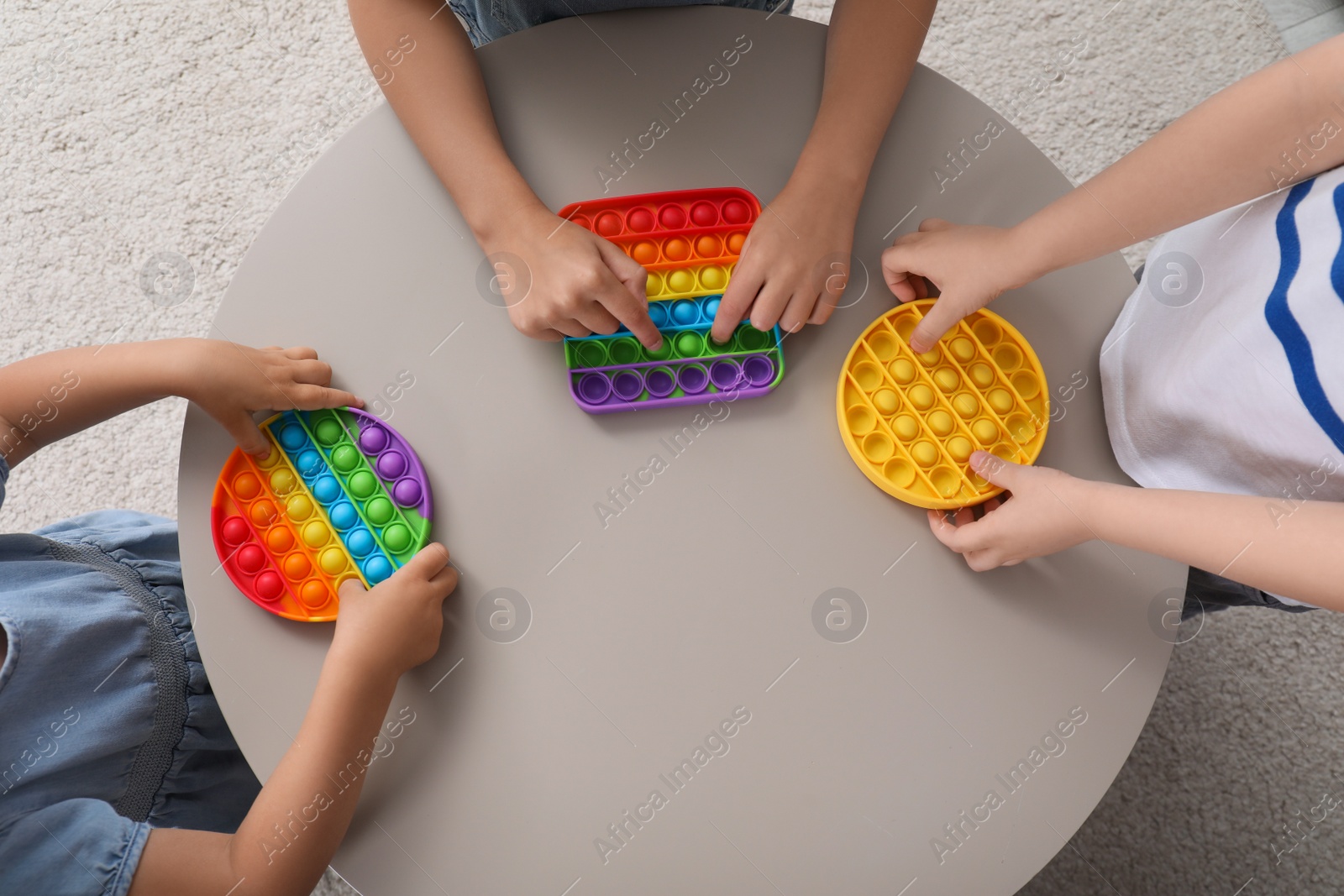 Photo of Little children playing with pop it fidget toys at table indoors, top view