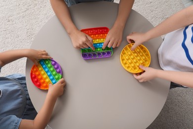 Little children playing with pop it fidget toys at table indoors, top view