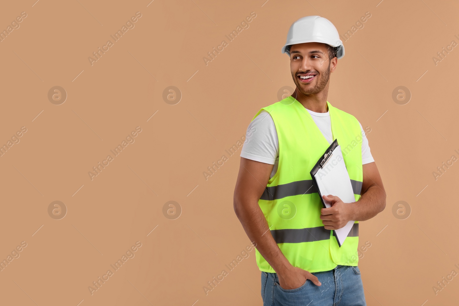 Photo of Engineer in hard hat holding clipboard on beige background, space for text