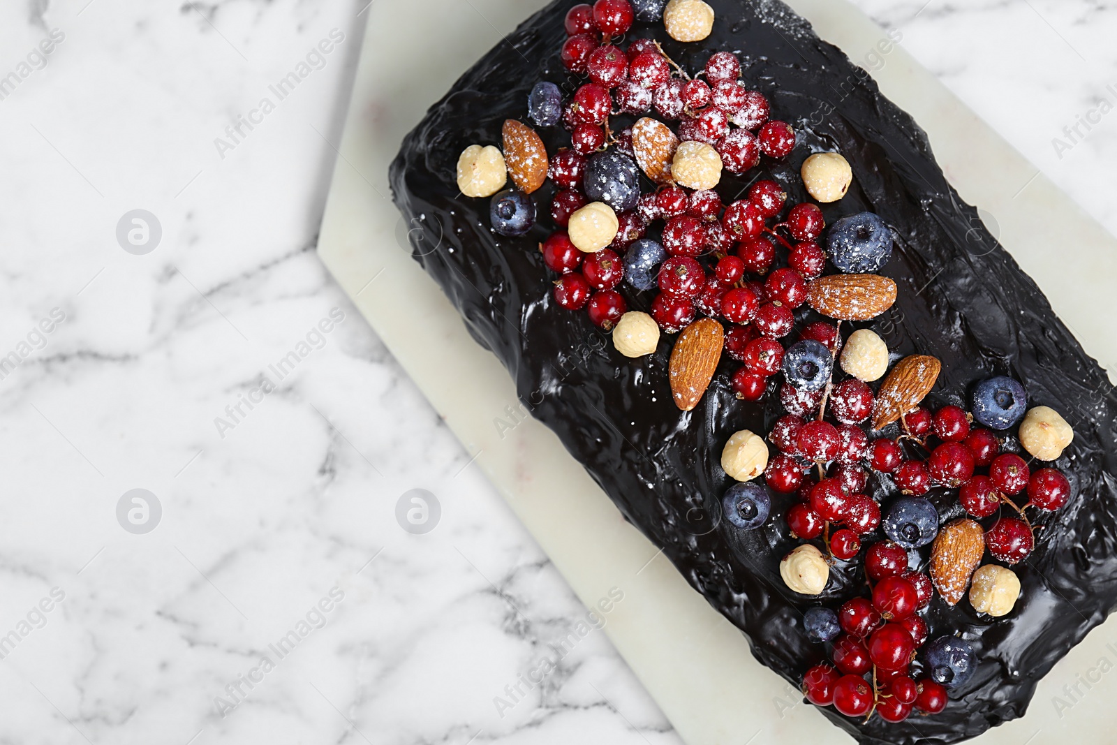 Photo of Delicious chocolate sponge cake with berries and nuts on white marble table, top view. Space for text