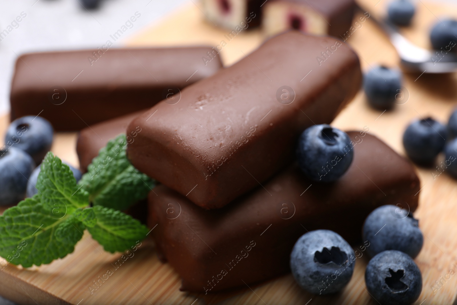 Photo of Delicious glazed curd snacks with fresh blueberries and mint on wooden board, closeup