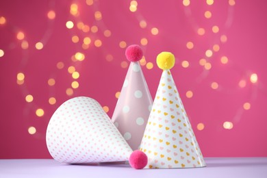 Party hats on violet table against pink background with blurred lights