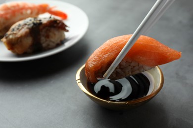 Photo of Dipping tasty nigiri sushi with salmon into soy sauce on grey table, closeup