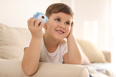 Little photographer with toy camera on sofa at home