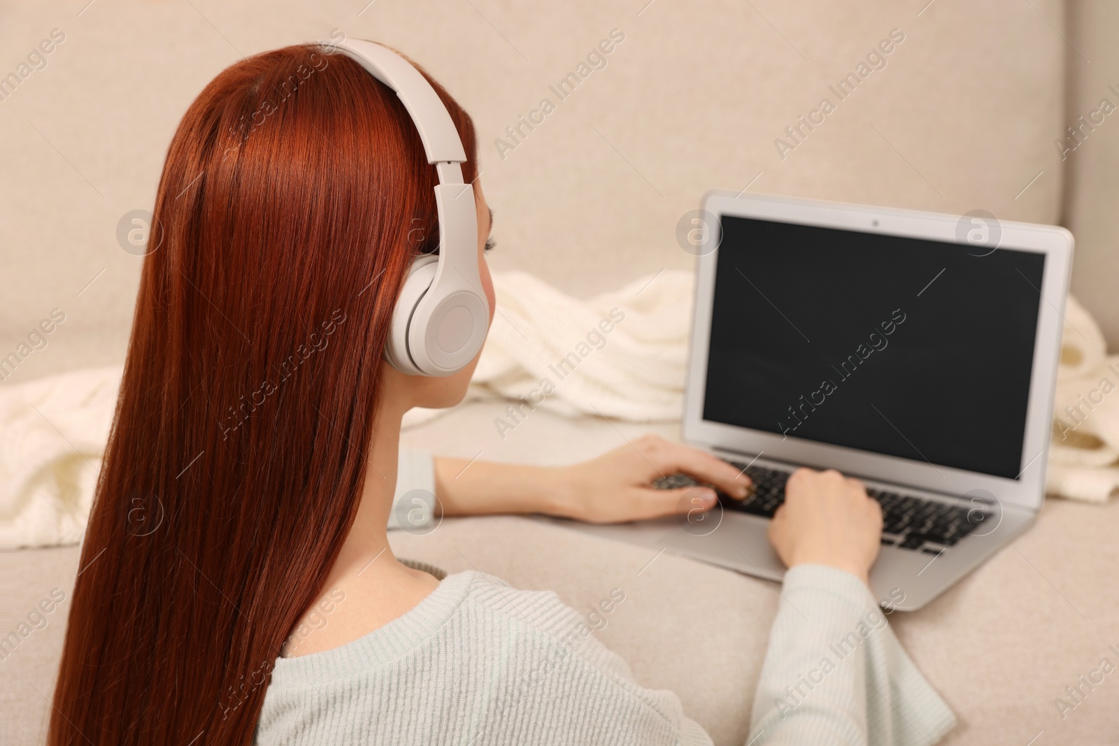 Photo of Woman with red dyed hair in headphone using laptop indoors