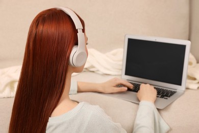 Woman with red dyed hair in headphone using laptop indoors