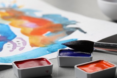Photo of Abstract watercolor painting, colorful paints and brush on grey table, closeup