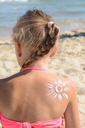 Photo of Little girl with sun protection cream on body near sea, back view