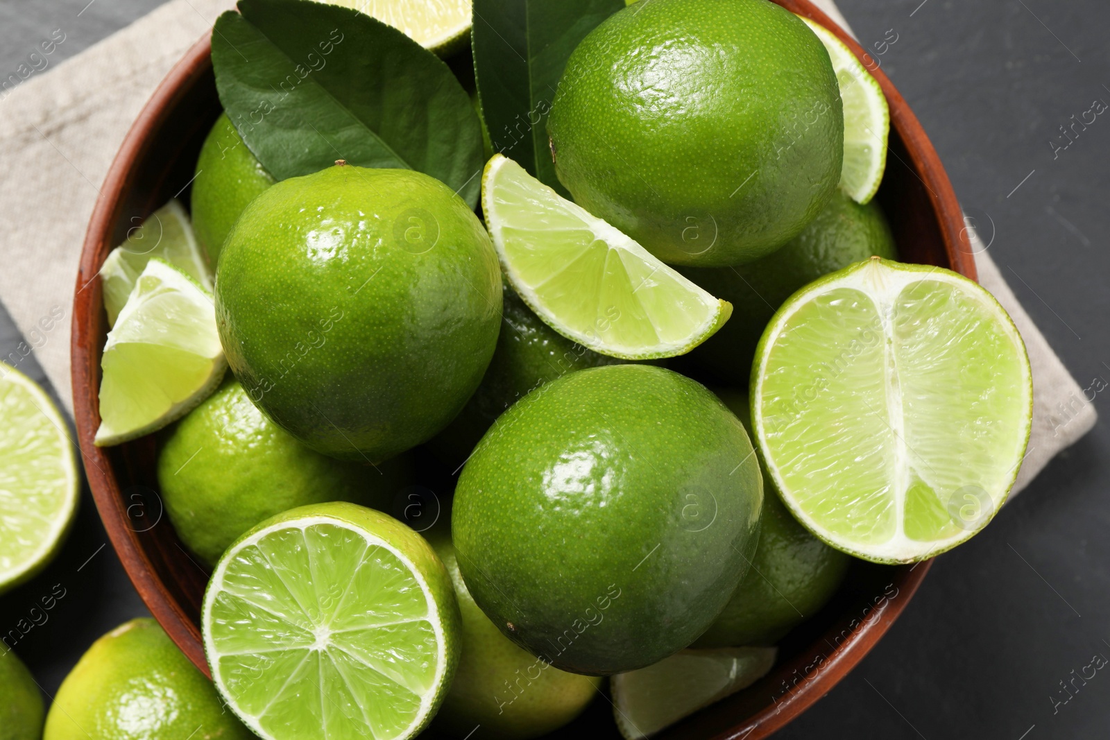 Photo of Fresh ripe limes in bowl on black table, top view