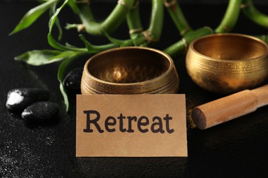 Photo of Card with word Retreat, singing bowls, spa stones and bamboo stems on wet black table