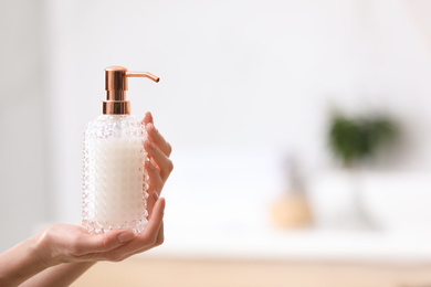 Woman holding soap dispenser on blurred background, closeup. Space for text