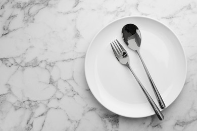 Photo of Clean plate and cutlery on white marble table, top view. Space for text