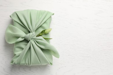 Furoshiki technique. Gift packed in green fabric and hellebore flower on white wooden table, top view with space for text
