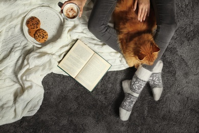 Woman with cute red cat and book on grey carpet, top view