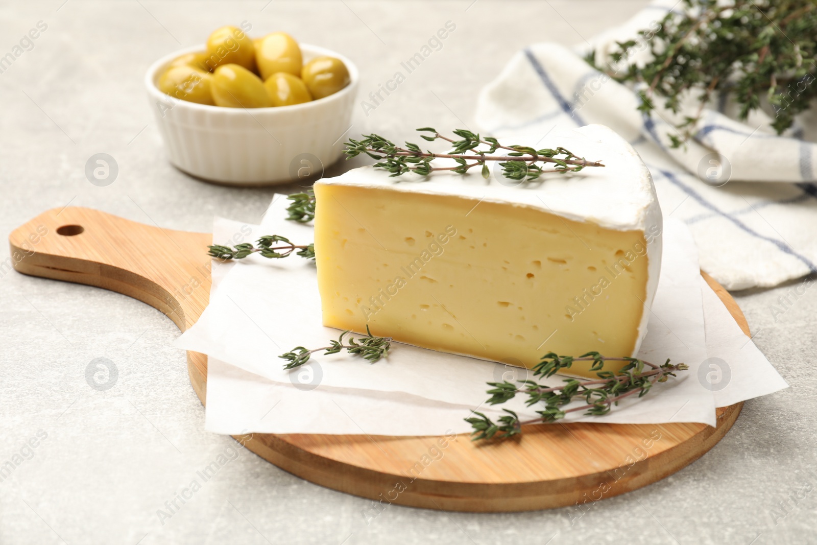 Photo of Piece of tasty camembert cheese and thyme on grey textured table, closeup