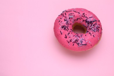 Photo of Glazed donut decorated with sprinkles on pink background, top view. Space for text. Tasty confectionery