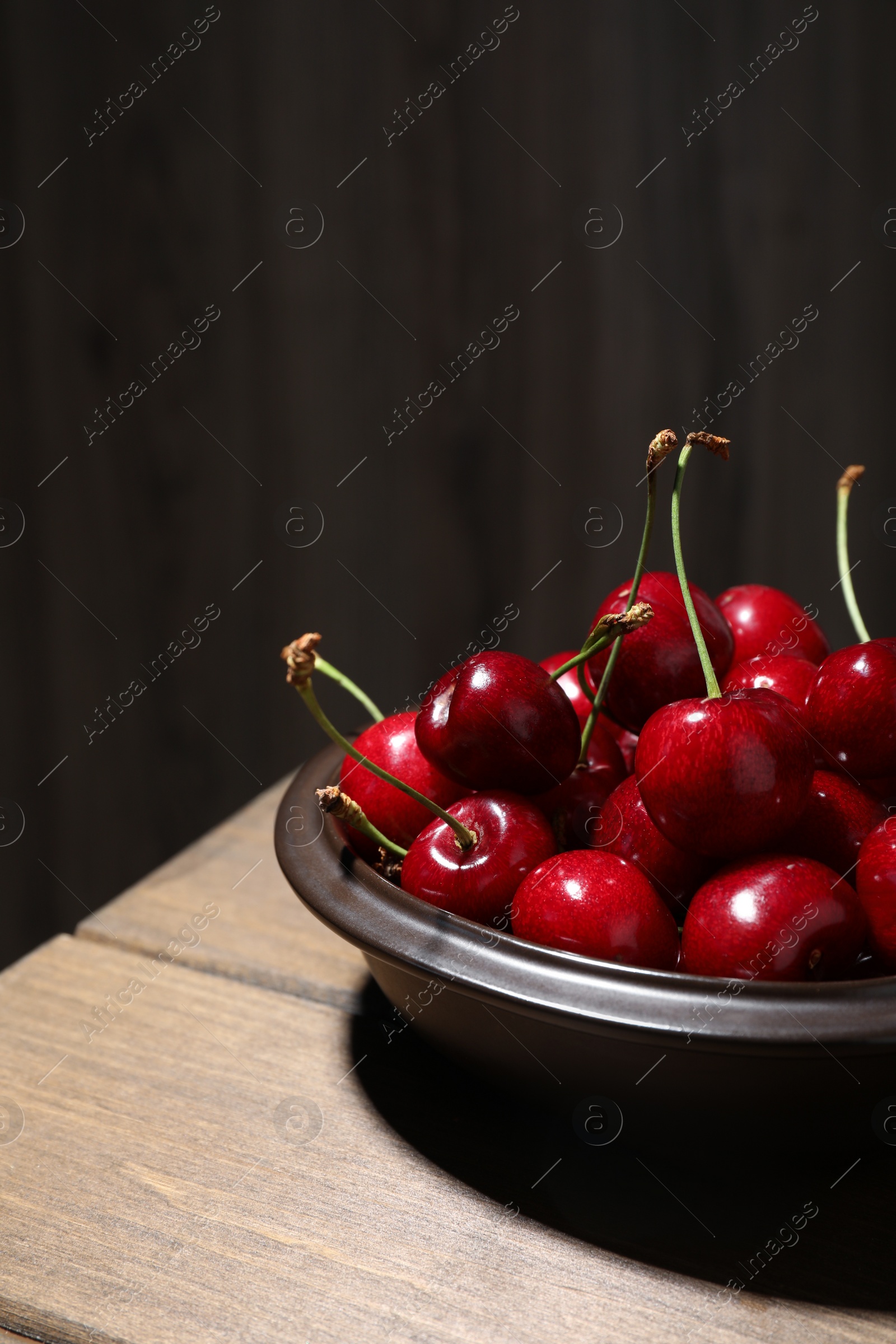 Photo of Sweet red cherries in bowl on wooden table, space for text