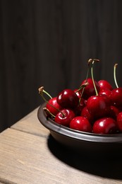 Photo of Sweet red cherries in bowl on wooden table, space for text