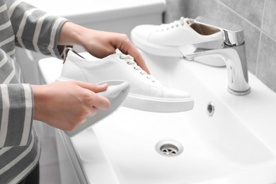 Photo of Woman washing stylish sneakers with brush in sink, closeup