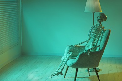 Waiting concept. Human skeleton sitting in armchair indoors, space for text