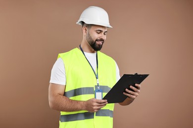 Photo of Engineer in hard hat holding clipboard on brown background