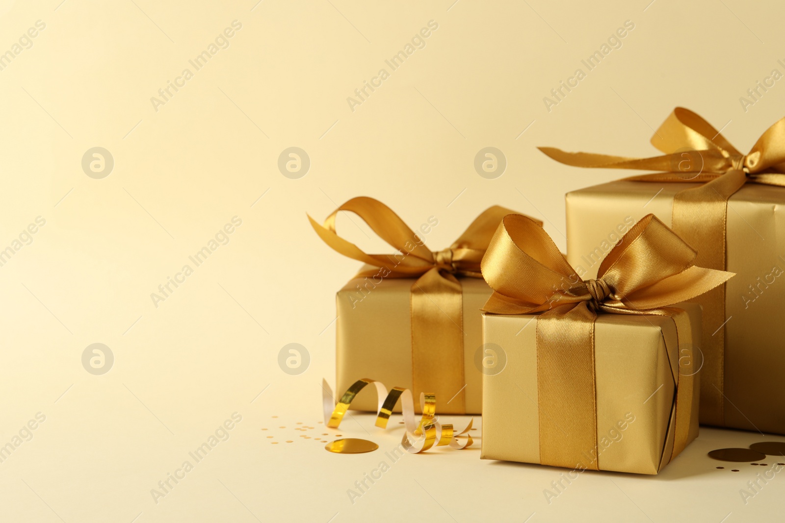 Photo of Beautifully wrapped gift boxes and confetti on beige background, space for text