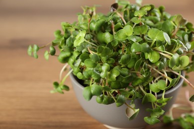 Photo of Fresh radish microgreens in bowl on wooden table, closeup. Space for text
