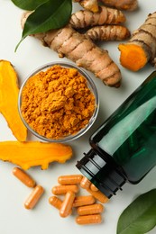 Aromatic turmeric powder, pills and raw roots on white table, flat lay