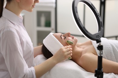 Photo of Cosmetologist making face massage with roller to client in clinic, closeup