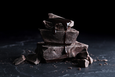 Pieces of tasty dark chocolate with syrup on black table, closeup